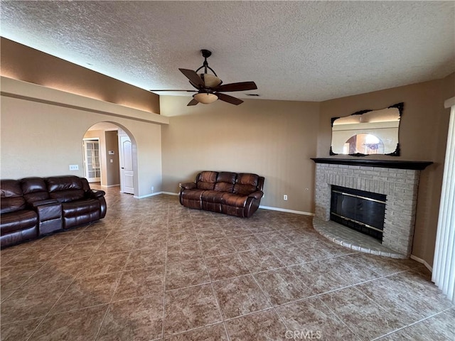 living room with ceiling fan, a fireplace, and a textured ceiling