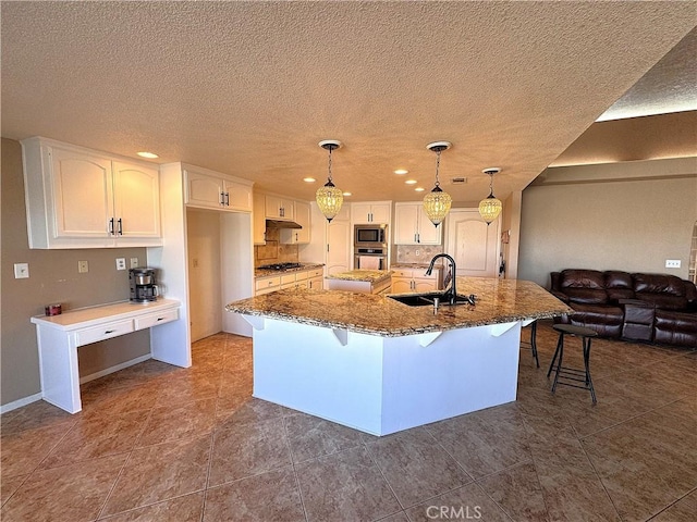 kitchen with a kitchen island with sink, white cabinets, sink, dark stone countertops, and stainless steel appliances