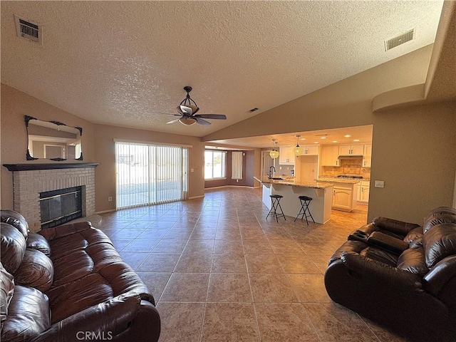 tiled living room featuring a fireplace, ceiling fan, a textured ceiling, and vaulted ceiling