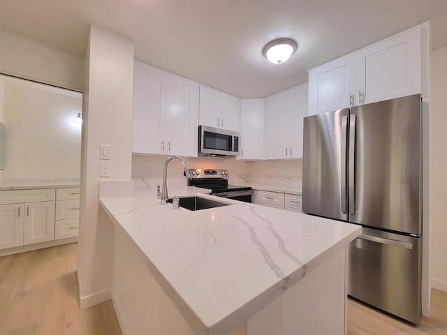 kitchen with light stone counters, stainless steel appliances, sink, light hardwood / wood-style flooring, and white cabinets