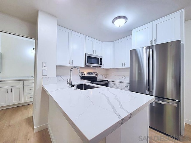 kitchen featuring sink, white cabinetry, stainless steel appliances, light stone countertops, and light wood-type flooring