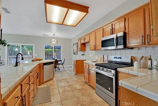 kitchen featuring decorative light fixtures, backsplash, stainless steel appliances, and tile counters