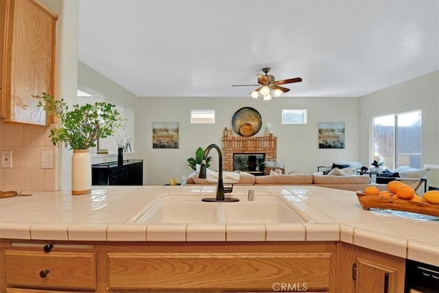 kitchen featuring ceiling fan, sink, a brick fireplace, backsplash, and tile countertops