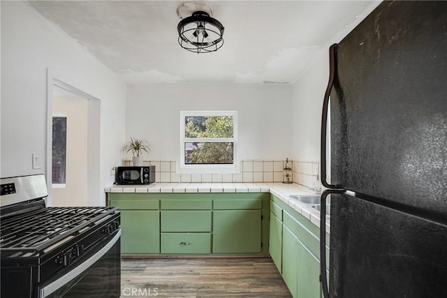 kitchen featuring black refrigerator, green cabinetry, light hardwood / wood-style flooring, stainless steel gas stove, and tile counters