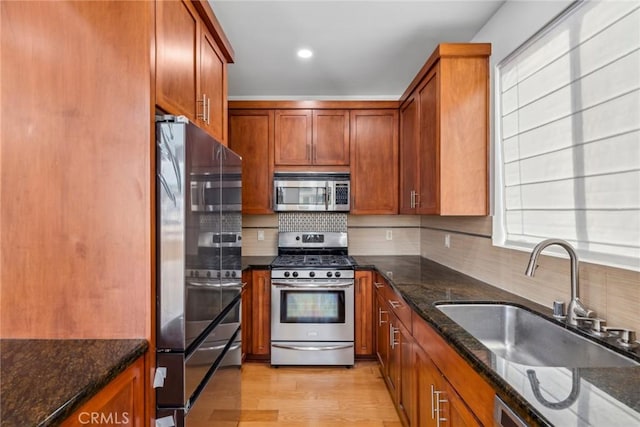 kitchen featuring appliances with stainless steel finishes, tasteful backsplash, dark stone counters, sink, and light hardwood / wood-style floors