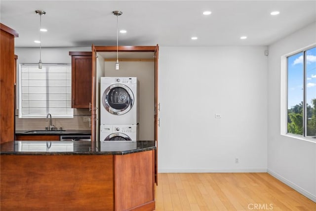 kitchen with stacked washing maching and dryer, sink, pendant lighting, dark stone countertops, and light hardwood / wood-style floors