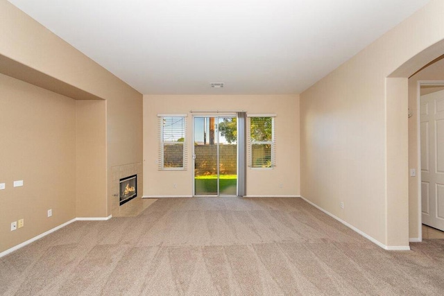 carpeted spare room featuring a tiled fireplace