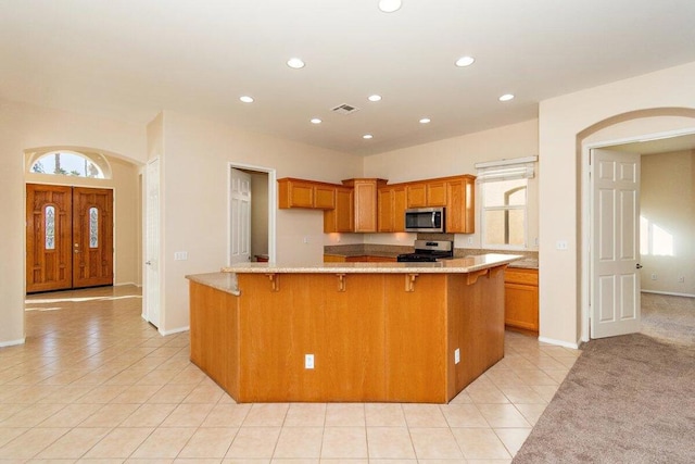 kitchen with a kitchen breakfast bar, light stone counters, light tile patterned floors, and appliances with stainless steel finishes