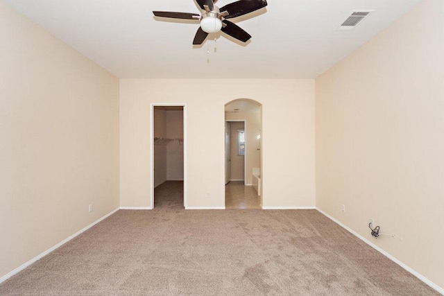 unfurnished bedroom featuring connected bathroom, ceiling fan, light colored carpet, a walk in closet, and a closet