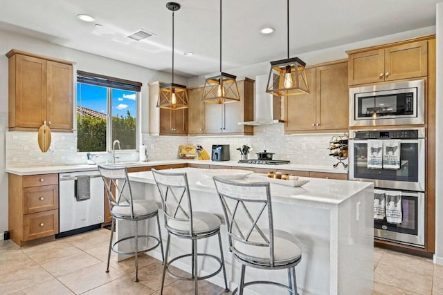 kitchen featuring appliances with stainless steel finishes, hanging light fixtures, decorative backsplash, a kitchen island, and wall chimney exhaust hood