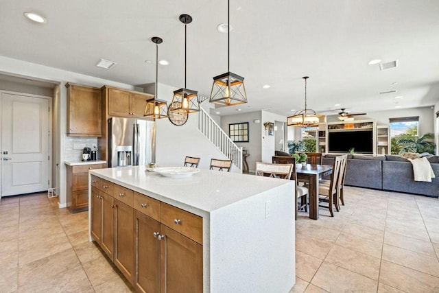 kitchen featuring pendant lighting, tasteful backsplash, stainless steel fridge with ice dispenser, light tile patterned floors, and a center island