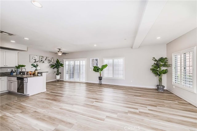 unfurnished living room featuring ceiling fan, a healthy amount of sunlight, beam ceiling, and light hardwood / wood-style flooring