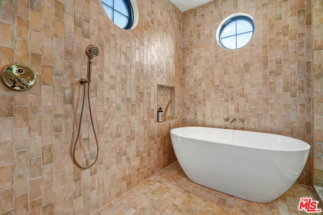 bathroom featuring a bath, a healthy amount of sunlight, and tile walls