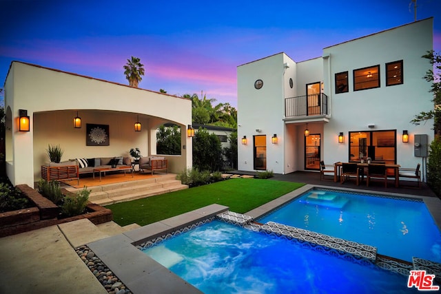 back house at dusk with a lawn, an outdoor living space, a balcony, and a patio