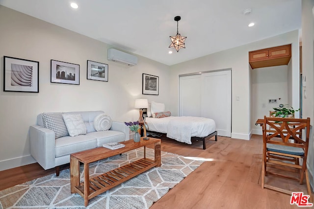 bedroom with a wall mounted AC, a closet, light hardwood / wood-style floors, and a notable chandelier