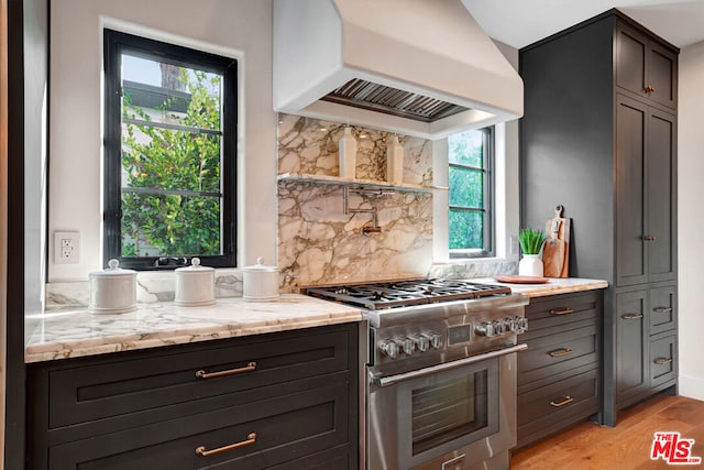 kitchen with light wood-type flooring, high end stove, premium range hood, and a wealth of natural light