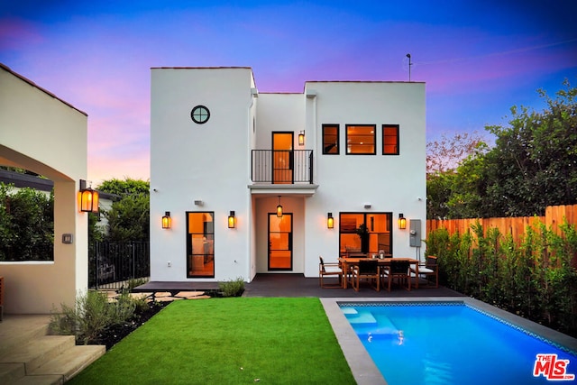 back house at dusk featuring a fenced in pool, a balcony, and a patio