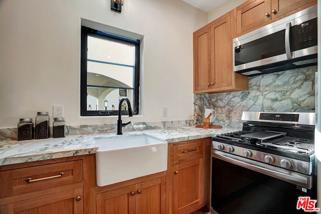 kitchen with light stone countertops, appliances with stainless steel finishes, backsplash, and sink