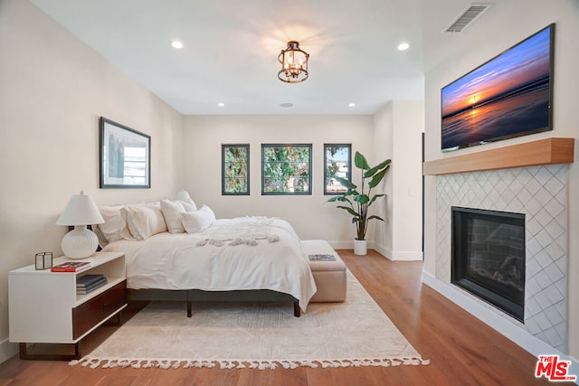 bedroom featuring a fireplace, a chandelier, and hardwood / wood-style flooring