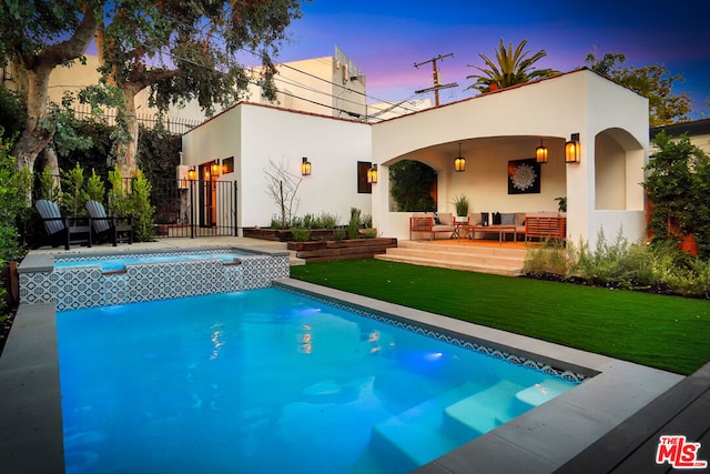 back house at dusk with outdoor lounge area, a pool with hot tub, a yard, and a patio