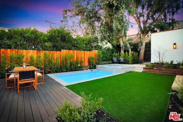 pool at dusk with a deck and a lawn