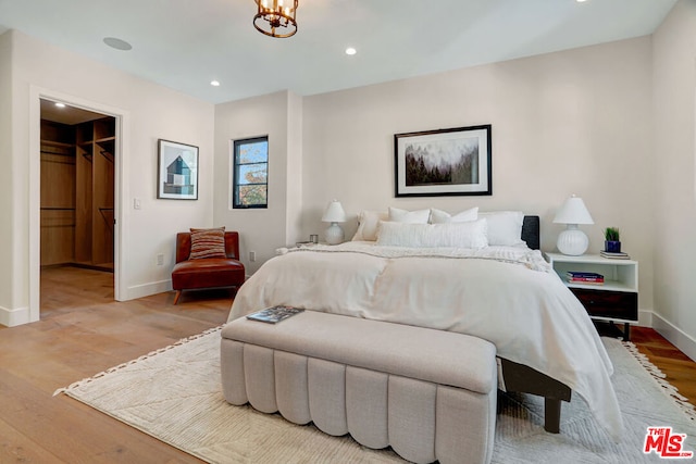 bedroom featuring a chandelier, light wood-type flooring, a walk in closet, and a closet