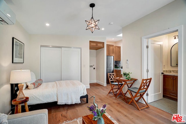 bedroom with stainless steel fridge, light wood-type flooring, ensuite bathroom, a wall unit AC, and a closet