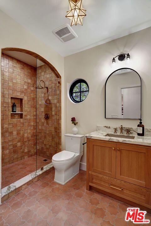 bathroom featuring a tile shower, vanity, and toilet