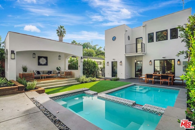 rear view of property with a yard, an outdoor living space, a balcony, and a patio