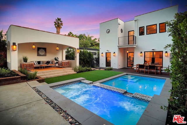 back house at dusk featuring outdoor lounge area, a balcony, a patio, and a pool with hot tub