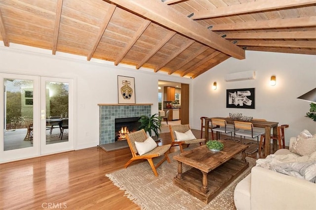 living room featuring french doors, lofted ceiling with beams, an AC wall unit, light hardwood / wood-style floors, and a tiled fireplace