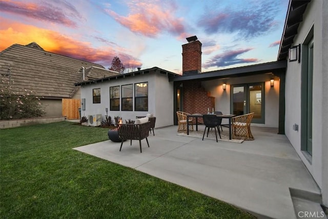 back house at dusk featuring a lawn and a patio area