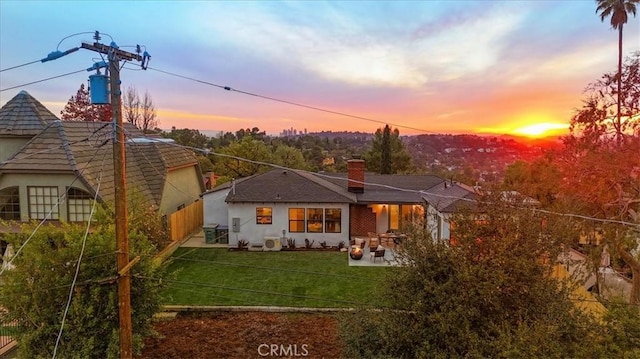 back house at dusk featuring a lawn and a patio area