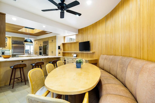 dining area featuring ceiling fan, sink, and wooden walls