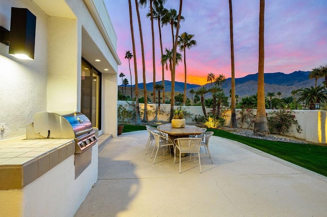 patio terrace at dusk featuring a mountain view, a grill, and an outdoor kitchen