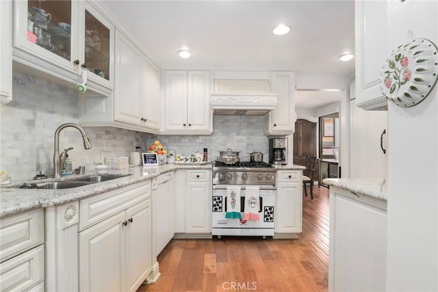 kitchen featuring custom exhaust hood, white cabinetry, sink, and high end range