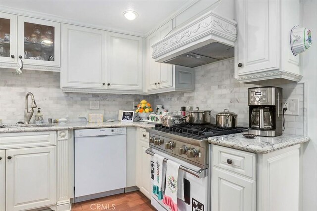 kitchen with custom exhaust hood, white cabinetry, stainless steel range, dishwasher, and backsplash