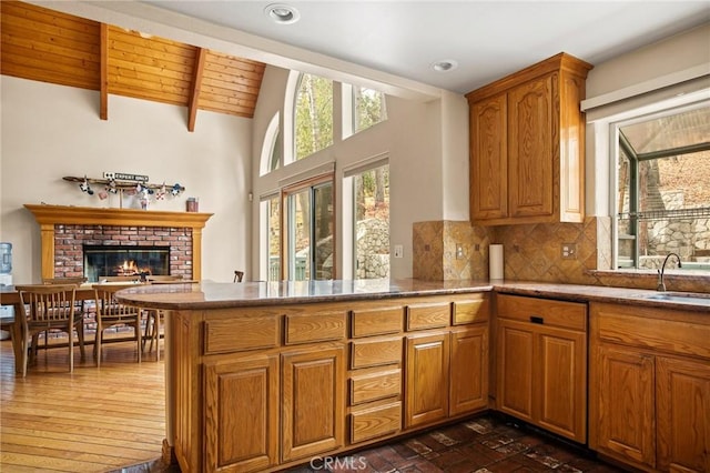 kitchen with sink, vaulted ceiling with beams, tasteful backsplash, a brick fireplace, and kitchen peninsula