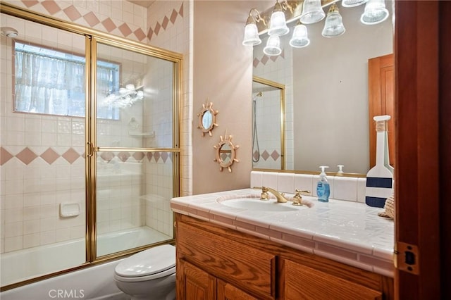 full bathroom featuring vanity, combined bath / shower with glass door, and toilet