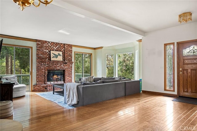 living room featuring beamed ceiling, a brick fireplace, a notable chandelier, and light hardwood / wood-style floors