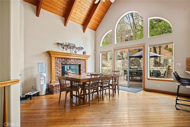 dining space with light hardwood / wood-style flooring, high vaulted ceiling, a brick fireplace, wooden ceiling, and beamed ceiling