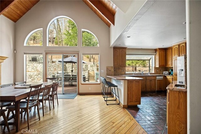 kitchen featuring tasteful backsplash, high vaulted ceiling, a kitchen breakfast bar, white fridge with ice dispenser, and hardwood / wood-style floors