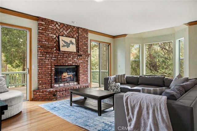 living room with a brick fireplace, crown molding, and light wood-type flooring