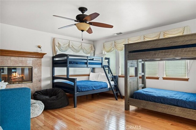 bedroom with ceiling fan, a high end fireplace, and hardwood / wood-style floors