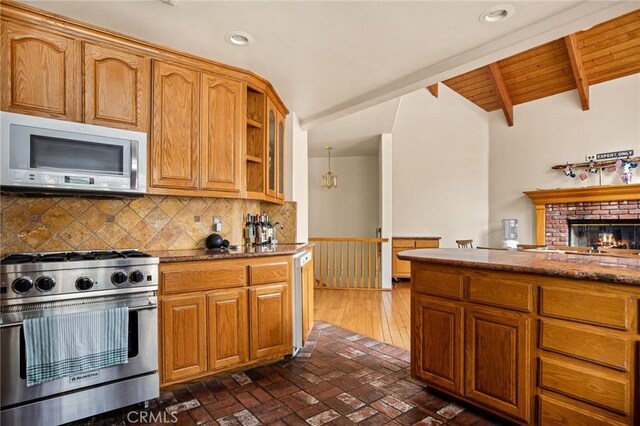 kitchen featuring lofted ceiling with beams, a brick fireplace, wooden ceiling, appliances with stainless steel finishes, and decorative backsplash