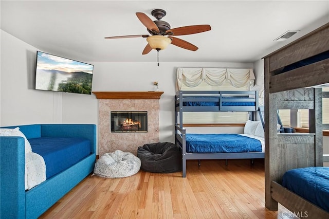 bedroom featuring hardwood / wood-style floors, a tile fireplace, and ceiling fan