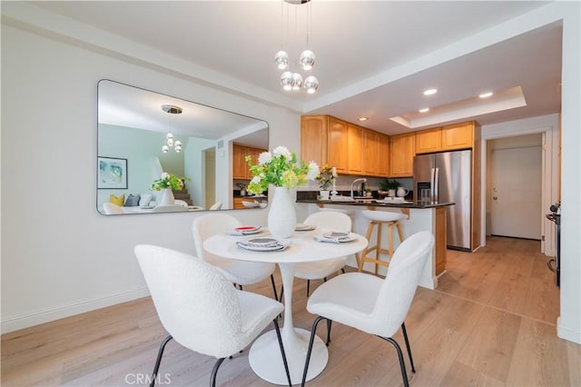 dining area featuring a tray ceiling, sink, light hardwood / wood-style floors, and an inviting chandelier