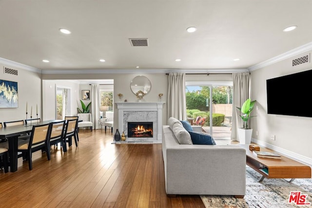 living room with hardwood / wood-style floors, crown molding, a healthy amount of sunlight, and a premium fireplace