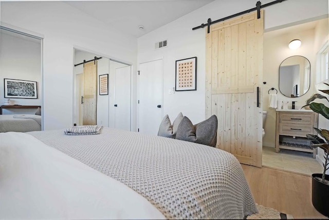 bedroom with lofted ceiling, a barn door, and light hardwood / wood-style flooring