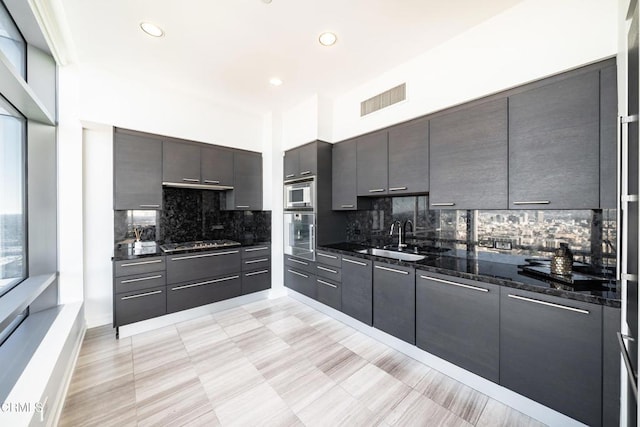 kitchen featuring sink, stainless steel appliances, backsplash, dark stone counters, and dark brown cabinets